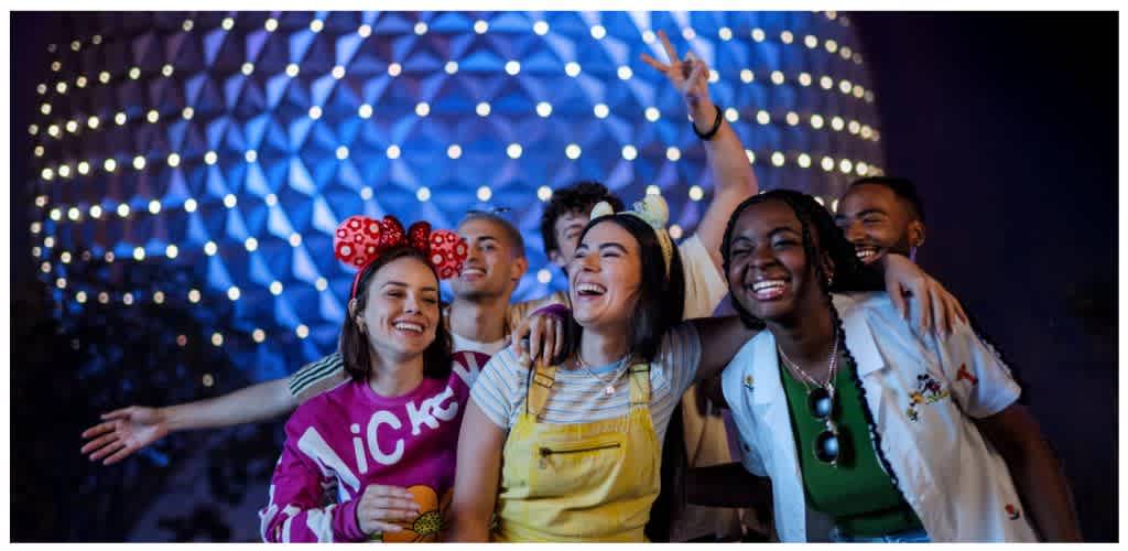 Group of diverse friends smiling and enjoying each other's company at a night event with colorful lights in the background
