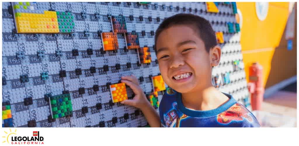 A child smiling and placing LEGO bricks on a large mosaic wall at LEGOLAND California.