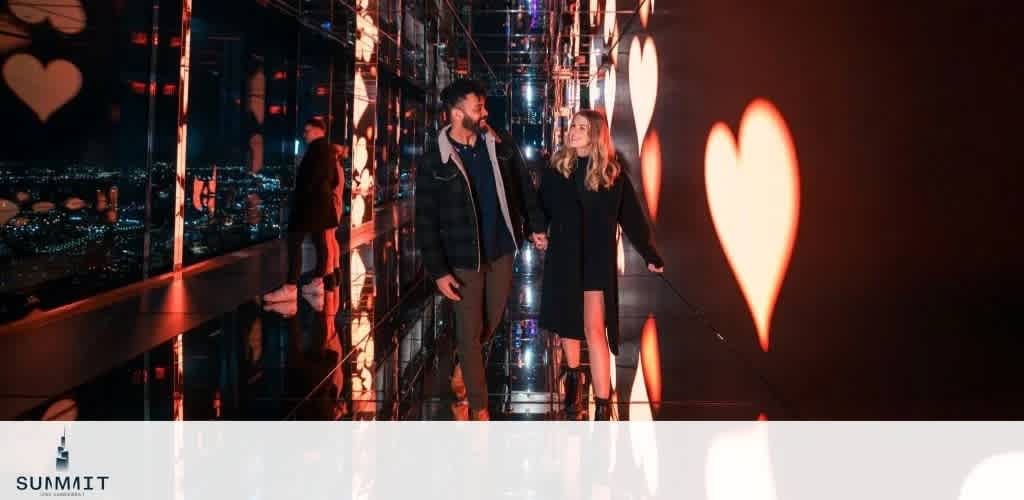 A couple walking hand in hand through a hallway with illuminated heart shapes on the wall and a city view.