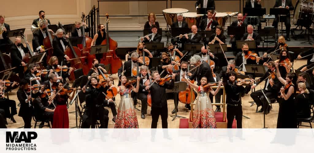 Orchestra performing on stage with musicians playing string, wind, and percussion instruments in a concert hall