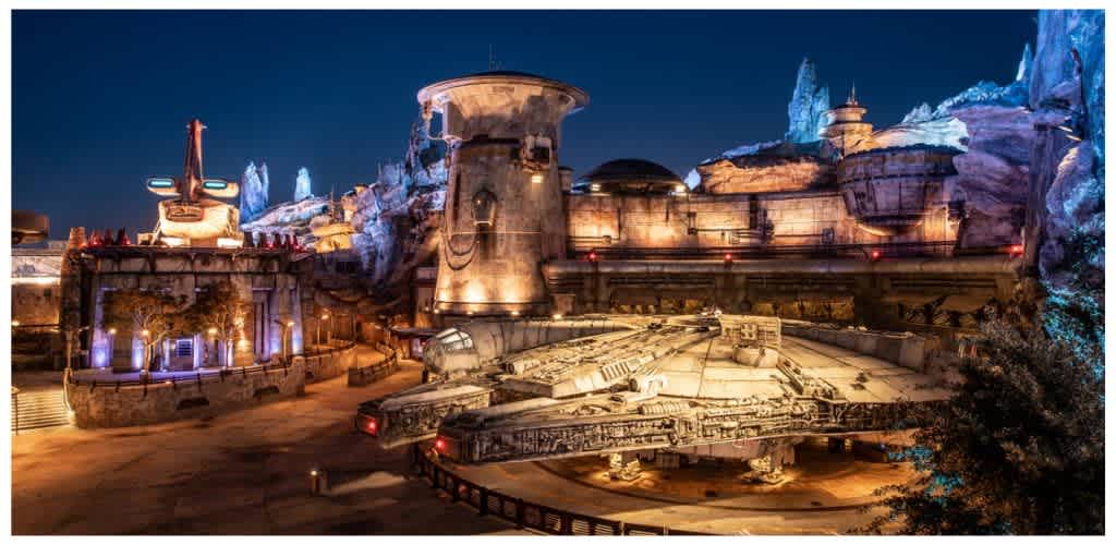 A nighttime scene of a Star Wars themed attraction featuring a large spaceship replica and futuristic structures illuminated with colorful lights