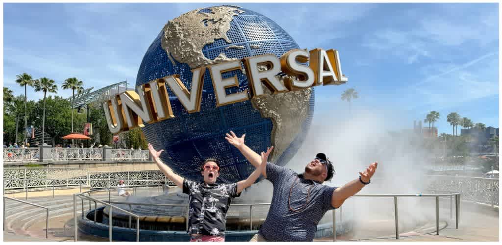 Two people pose excitedly in front of the Universal Studios globe with the Universal logo prominently displayed behind them.
