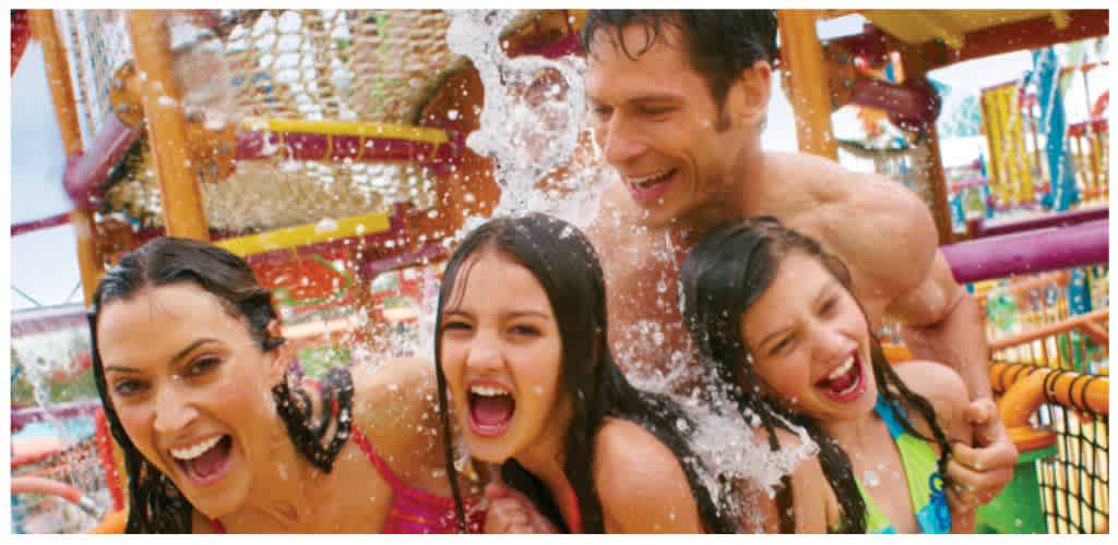 A family enjoys playing and splashing in a colorful water park on a sunny day.