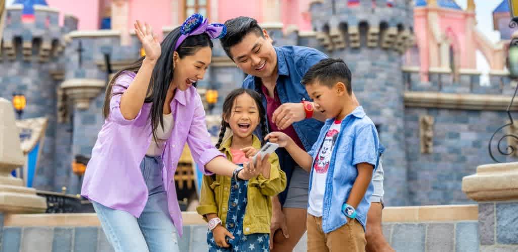 A family of four enjoying a fun moment together at a theme park with a castle in the background
