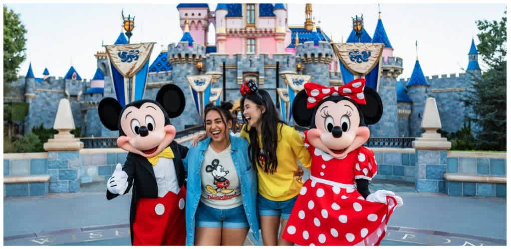 Two women smile with Mickey and Minnie Mouse characters in front of a castle at Disneyland theme park