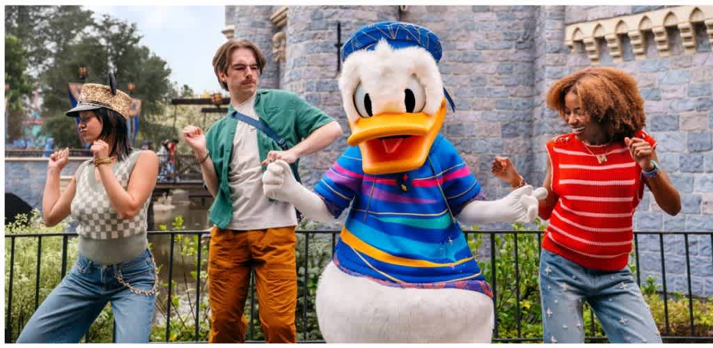 People dancing with Donald Duck mascot at a Disney theme park with castle in background.