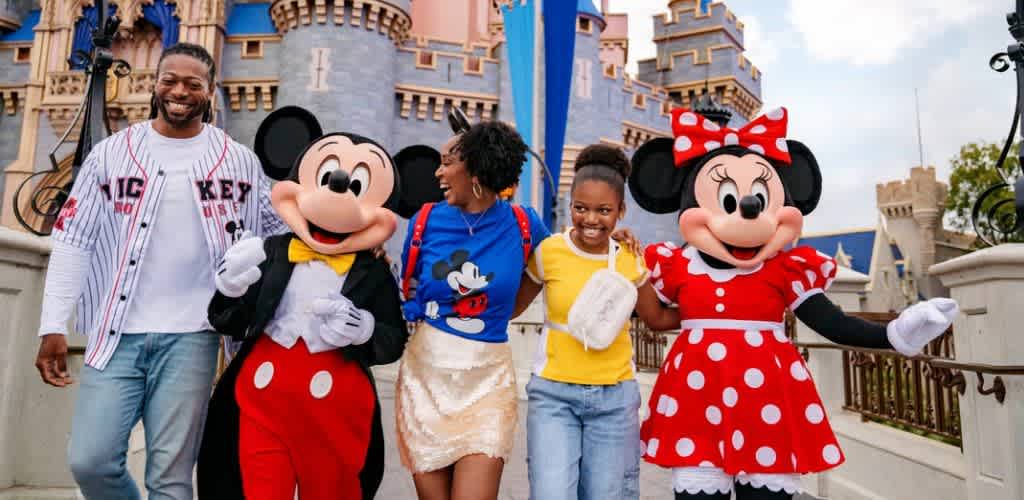 A group of people dressed as Mickey and Minnie Mouse along with two guests standing in front of a themed castle at a Disney park.