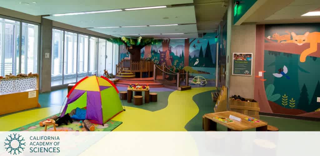 Children's play area with a colorful tent, toys, and a nature-themed mural.