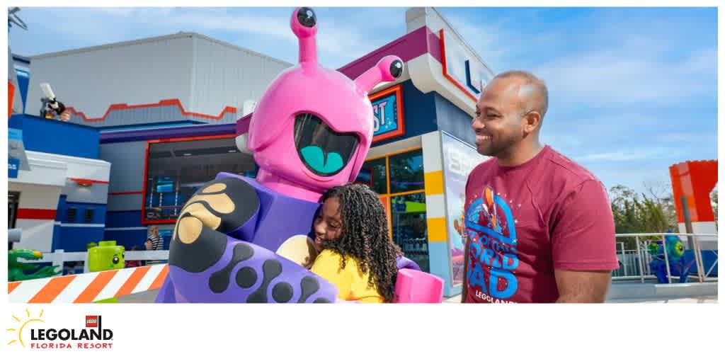 A child hugs a pink alien character at LEGOLAND Florida Resort, with a smiling adult nearby.