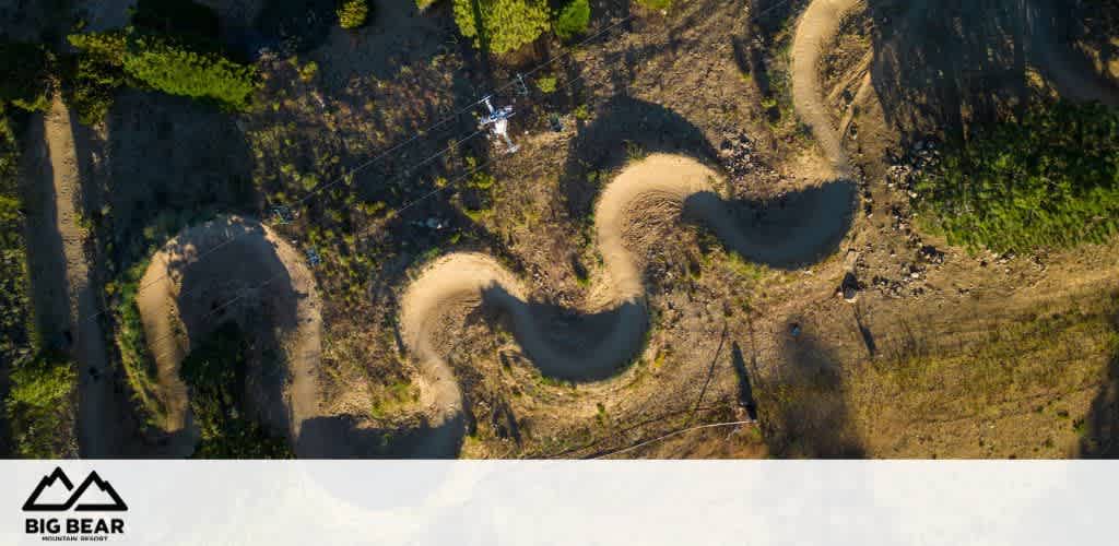 Aerial view of a dirt mountain bike trail with sharp turns and greenery surrounding the path