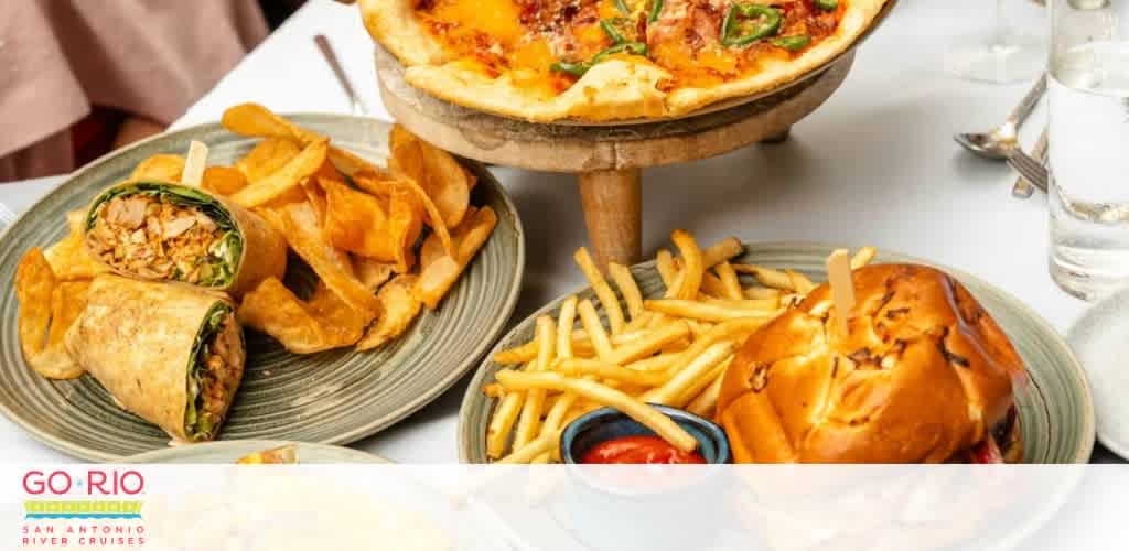 Dining table with pizza, chicken wrap with chips, and a burger with fries.