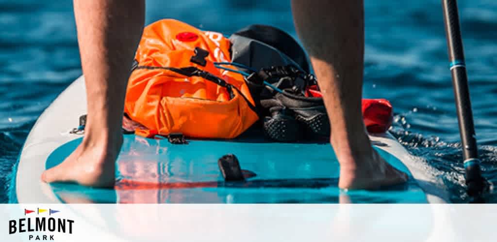 A person paddleboarding on blue water with an orange dry bag on the board.
