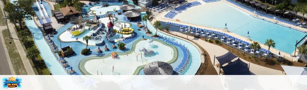 Aerial view of a large water park with multiple pools, lazy rivers, water slides, and lounge areas all surrounded by palm trees and shaded umbrellas