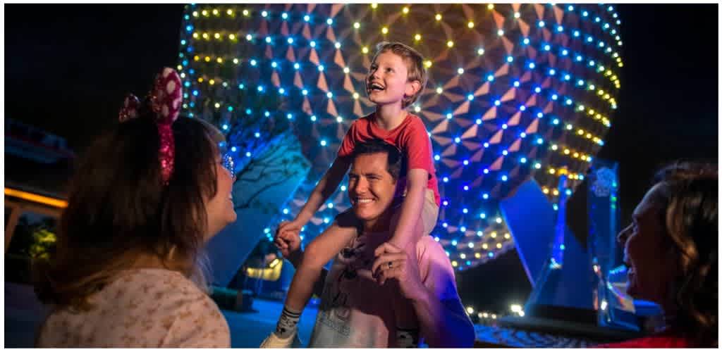 A group of people enjoying a night at an amusement park with colorful illuminated structures in the background.