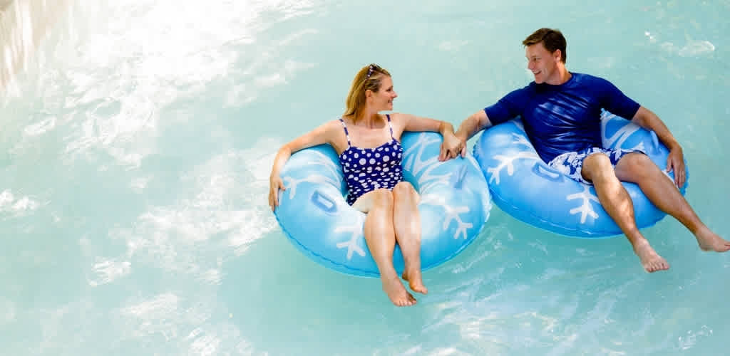A man and a woman enjoy a relaxing moment on floaties in a swimming pool holding hands and smiling at each other.