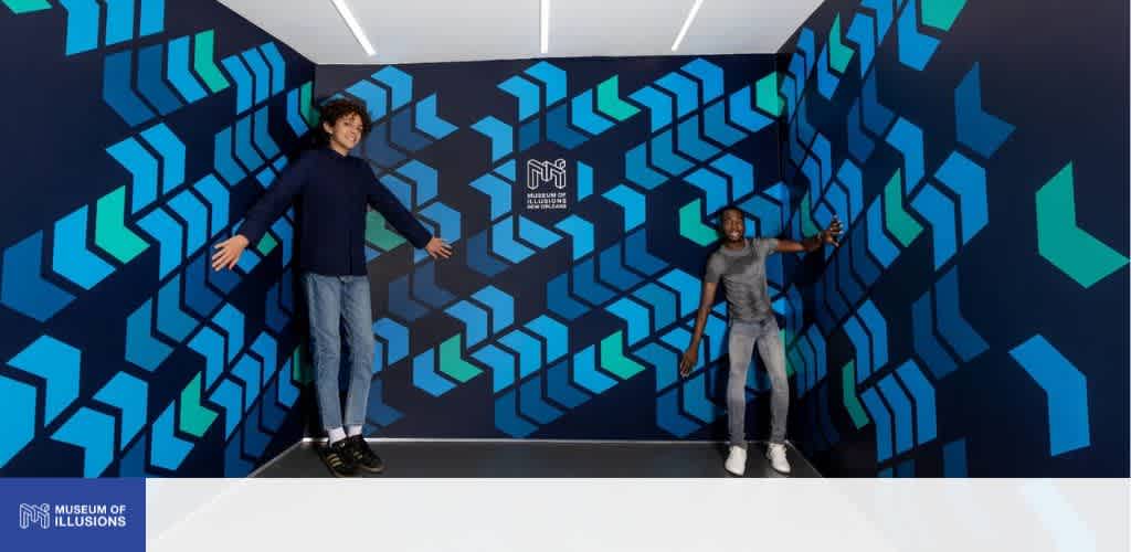 Two boys posing inside the Ames Room at Museum of Illusions New Orleans with blue geometric arrow patterns on the walls