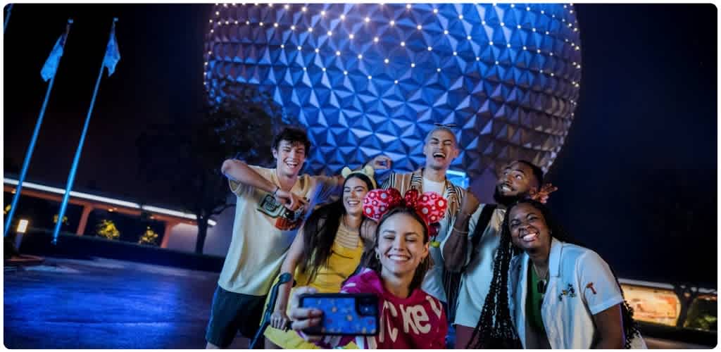 Group of friends smiling and posing for a selfie in front of Spaceship Earth lit up at night at EPCOT, Walt Disney World Resort.