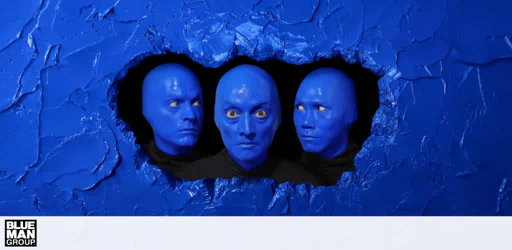 Three individuals with blue-painted faces and black clothing emerge through a jagged hole in a blue textured wall.