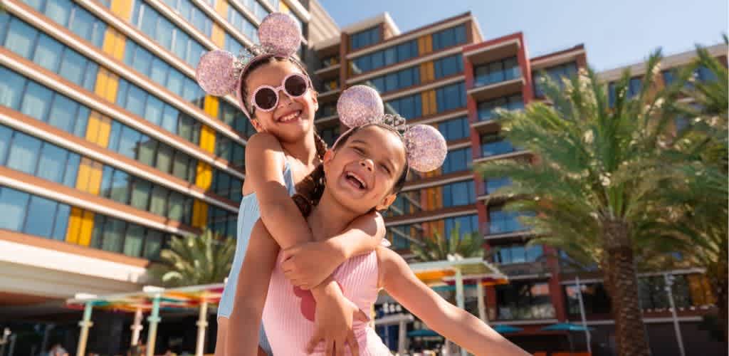 Two little girls wearing Mickey ears hugging happily at Disneyland Resort during summer.