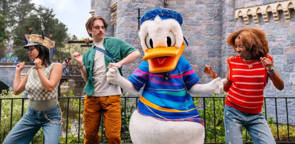 Young guests dancing with Donald Duck in front of Sleeping Beauty Castle at Disneyland.