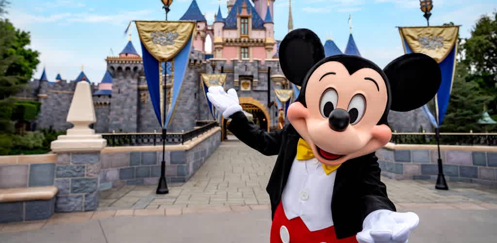 Mickey Mouse in a tuxedo posing in front of Sleeping Beauty Castle at Disneyland Resort.
