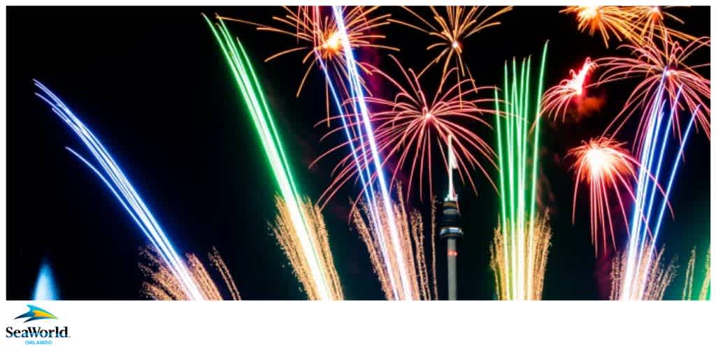 Colorful fireworks illuminate a dark sky, bursting in various colors around a central tower, with a SeaWorld Orlando logo in the bottom left corner.