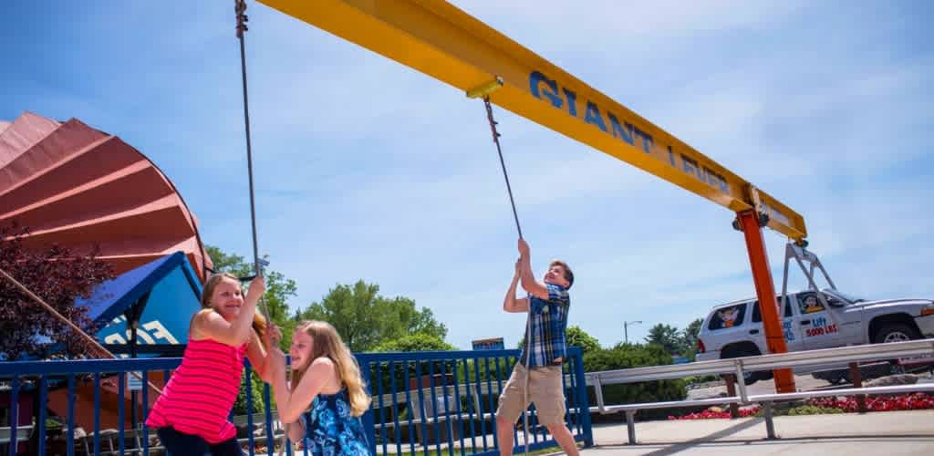 Children playing on a swing set at an amusement park with a large yellow crane and a white vehicle in the background