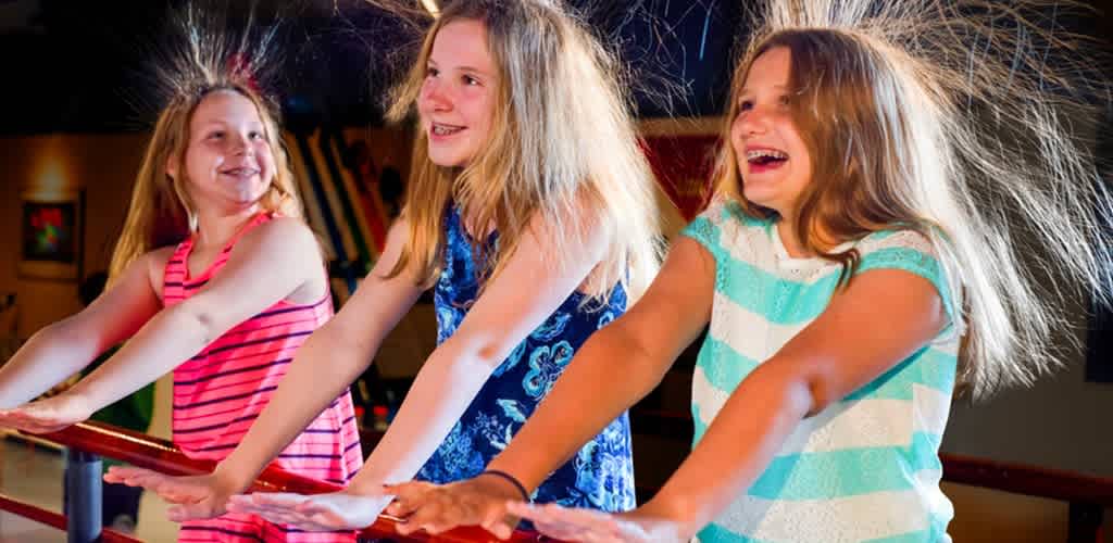 Three smiling girls with long hair having fun on an indoor amusement ride or attraction.