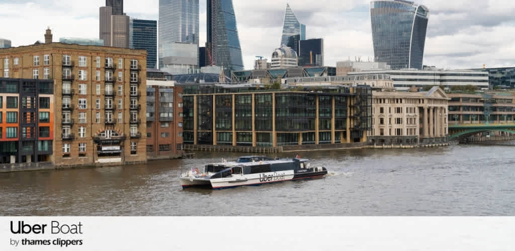 A boat with Uber Boat branding sailing on a river with modern and historic buildings in London's skyline.