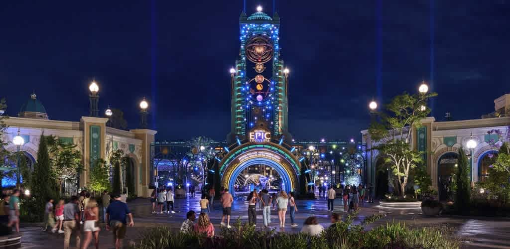 People walking around the entrance arc of Epic Universe at night.