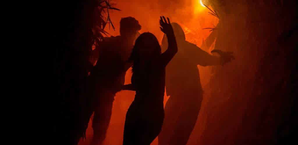 Silhouettes of children dancing in a fiery orange and red burning forest background during a Halloween event