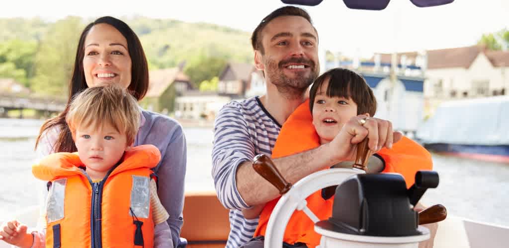 A family with two children enjoying a boat ride on the water with life jackets, outdoors on a sunny day.