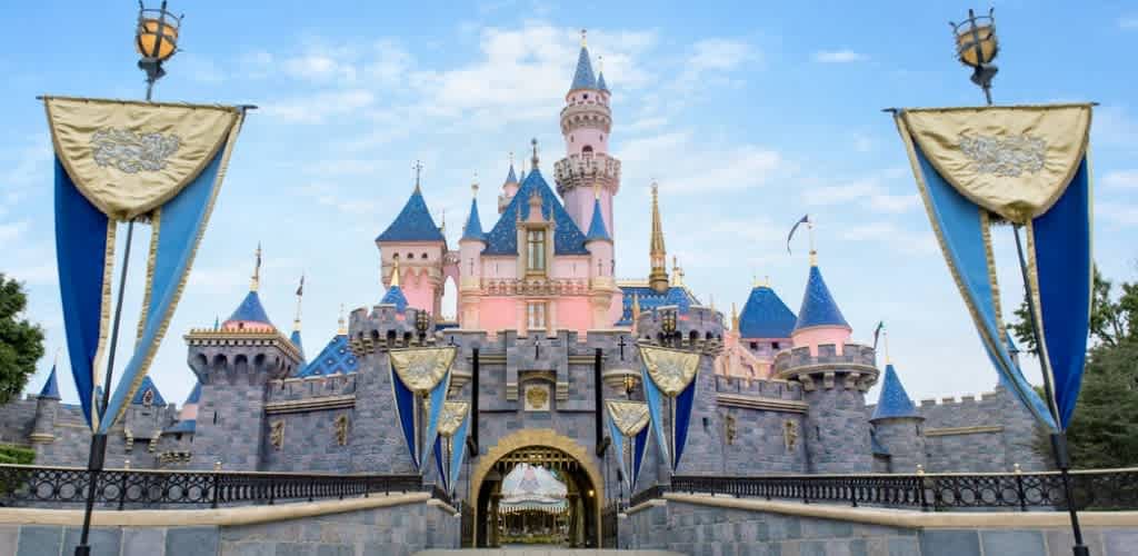 A view of Sleeping Beauty Castle at Disneyland with pink and blue turrets, flags, and banners in front.