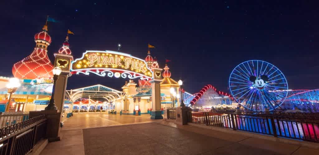 Night view of Pikzar Pier with illuminated amusement rides and a Mickey Mouse Ferris wheel at an empty theme park.
