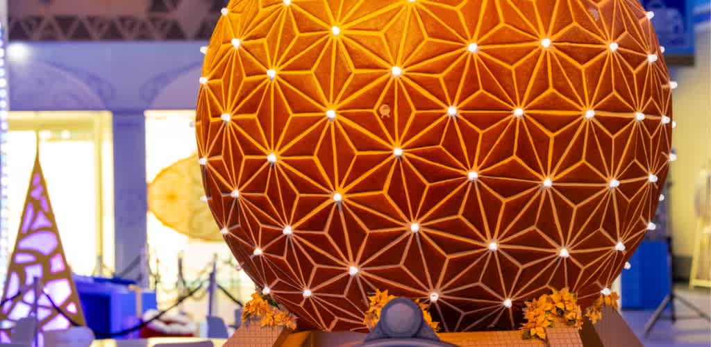 A large spherical geometric sculpture with glowing white lines forming interconnected triangles and orange flowers at its base