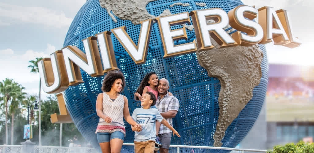 A family of four standing happily in front of the universal globe sign at Universal Studios theme park.