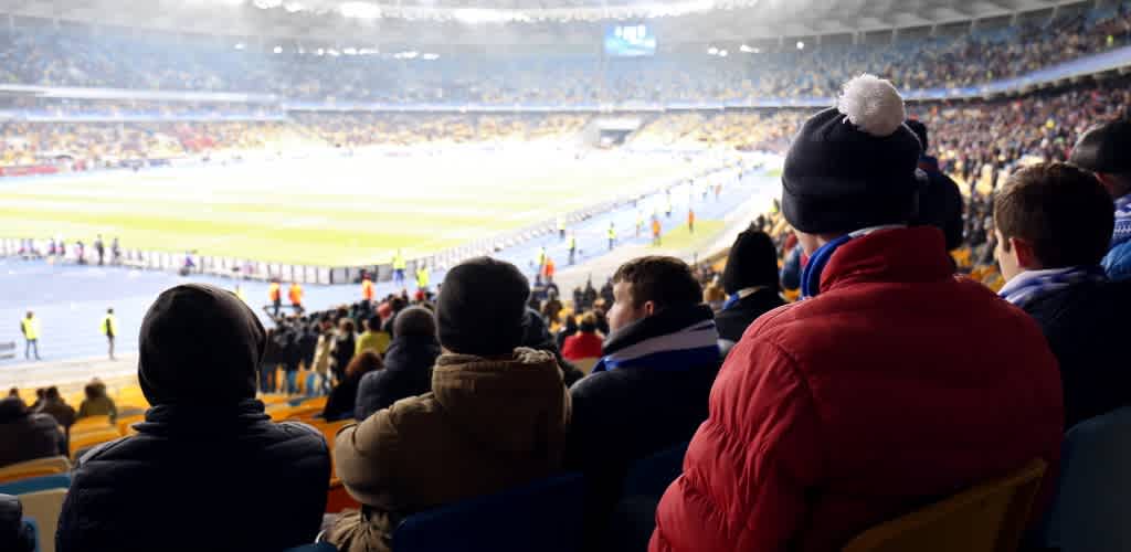 Crowd watching a sports game in a stadium with spectators dressed warmly in winter clothing.