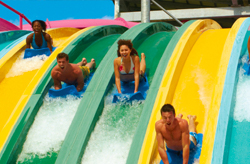 Four people joyfully sliding down colorful water slides.