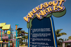 Sign for "Walkabout Waters" with safety rules at a colorful water park on a sunny day.