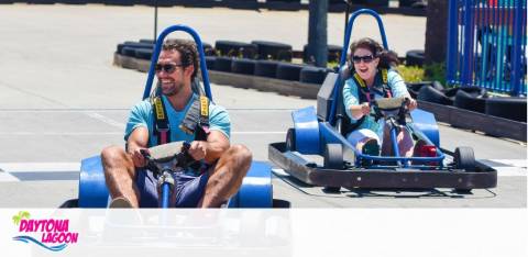 Two people enjoy a sunny day racing in go-karts on an outdoor track.