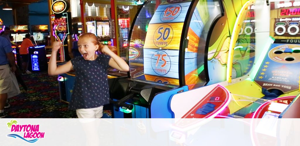 Girl excited in an arcade with colorful game machines visible.