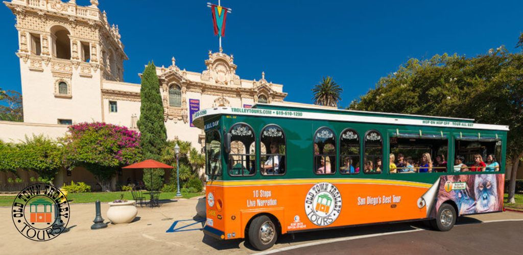 Image shows a vibrant orange and green trolley with passengers, marked 'Old Town Trolley Tours', in front of a historical ornate building with towers, under clear blue skies. Landscaping with greenery and flowering shrubs enhances the scene.