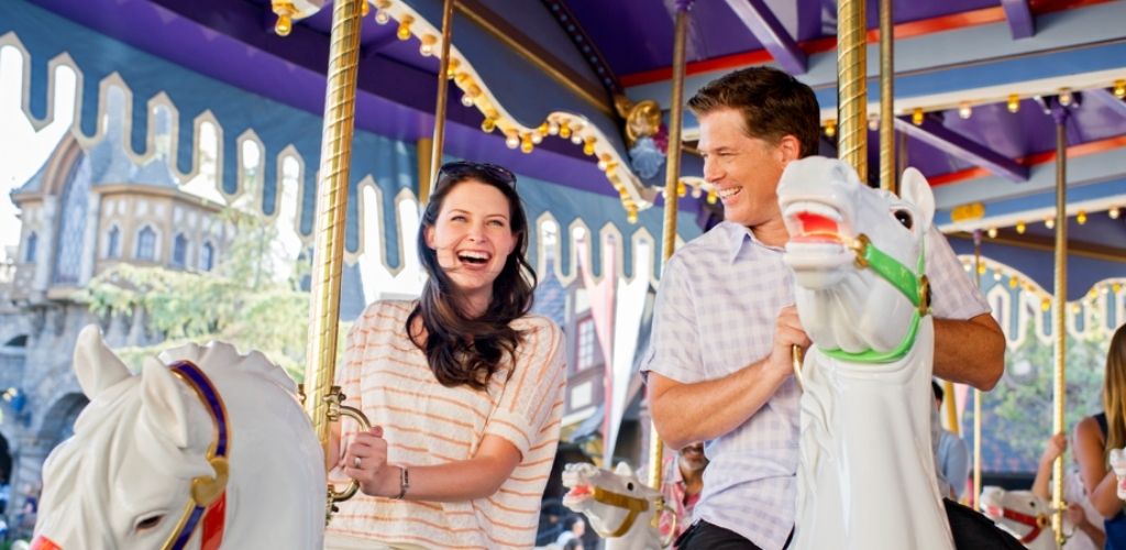 A couple laughing and enjoying a ride on King Arthur Carrousel at Disneyland Park.