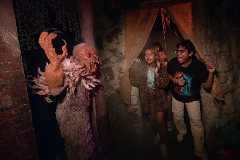 A group of people in Halloween costumes stands nervously in front of a creepy clown, adding to the spooky atmosphere.