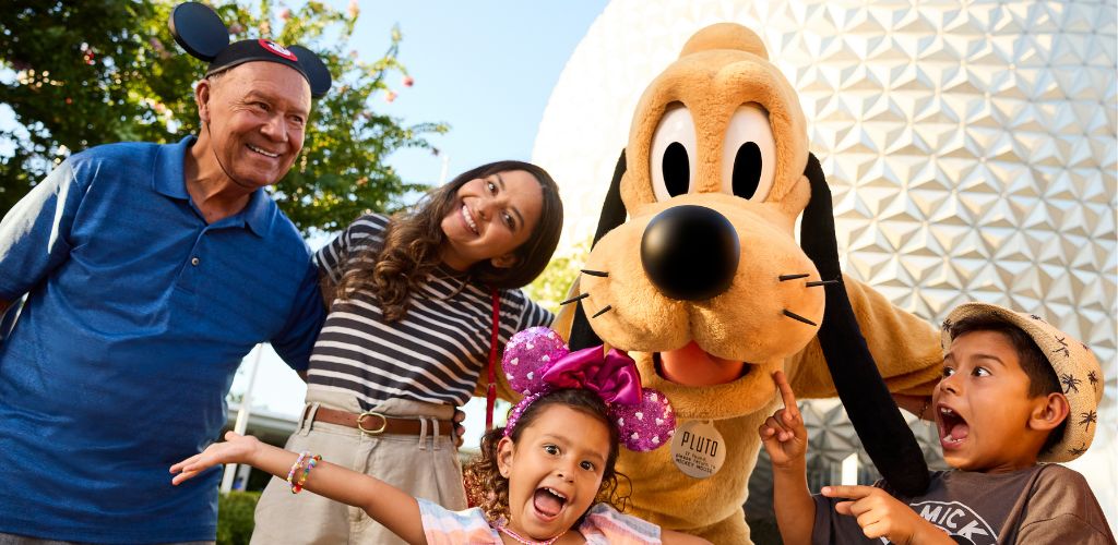 People smiling and interacting with a person in a Pluto costume outdoors at an amusement park