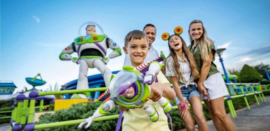 A family of four enjoying a themed amusement park with Toy Story characters and attractions on a sunny day