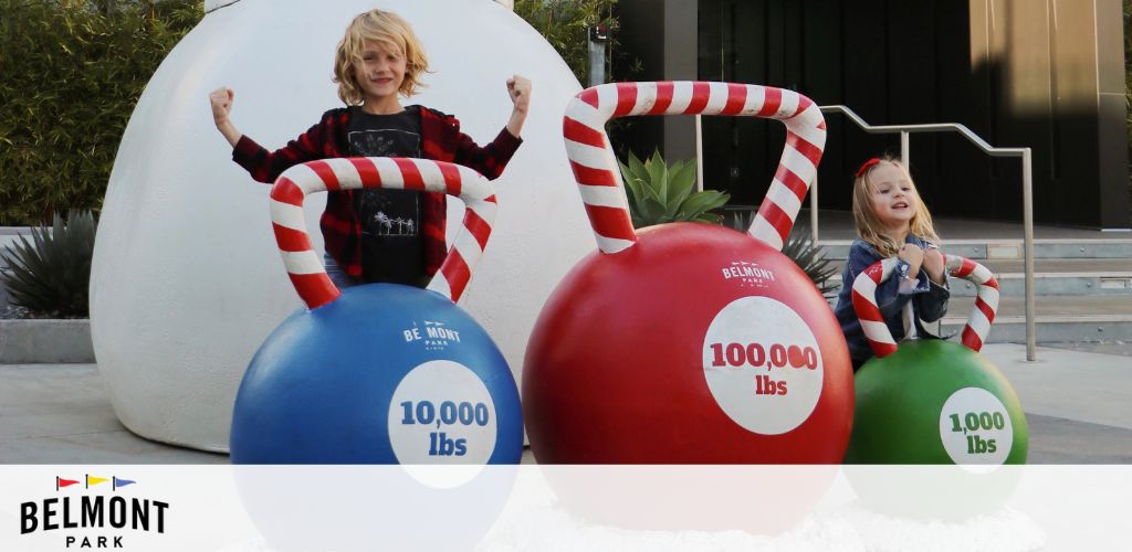 Children posing with oversized kettlebell-shaped ornaments at Belmont Park.