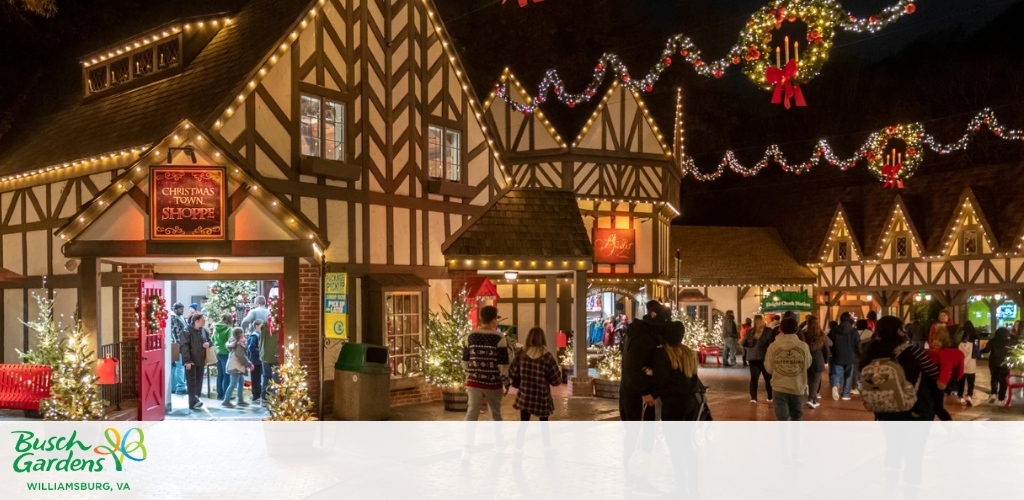 Tudor-style buildings decorated with Christmas lights and wreaths at night, with people walking around.