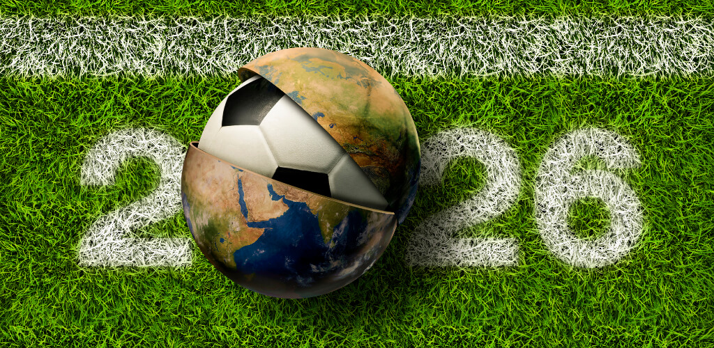 A soccer ball designed like Earth resting on a green field with '2026' painted on the grass, representing the 2026 FIFA World Cup.