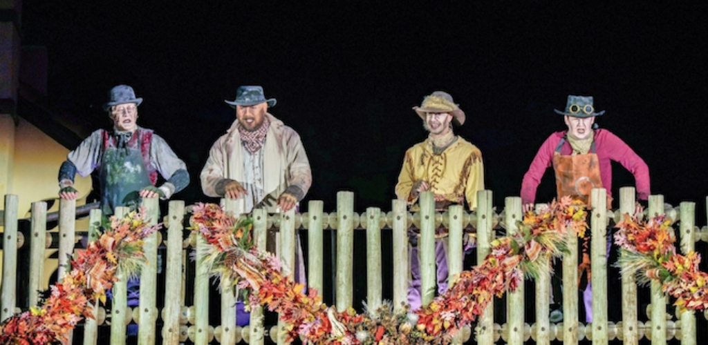 The Cadaver Dans performers in old-timey ghostly cowboy costumes standing behind a fall-decorated fence at Magic Kingdom Park.